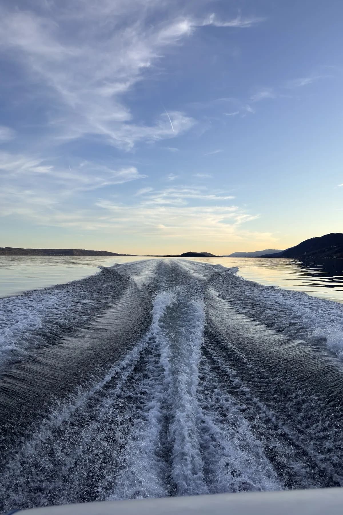 Kielwasser hinter einem Boot, dahinter eine Insel im Gegenlicht.